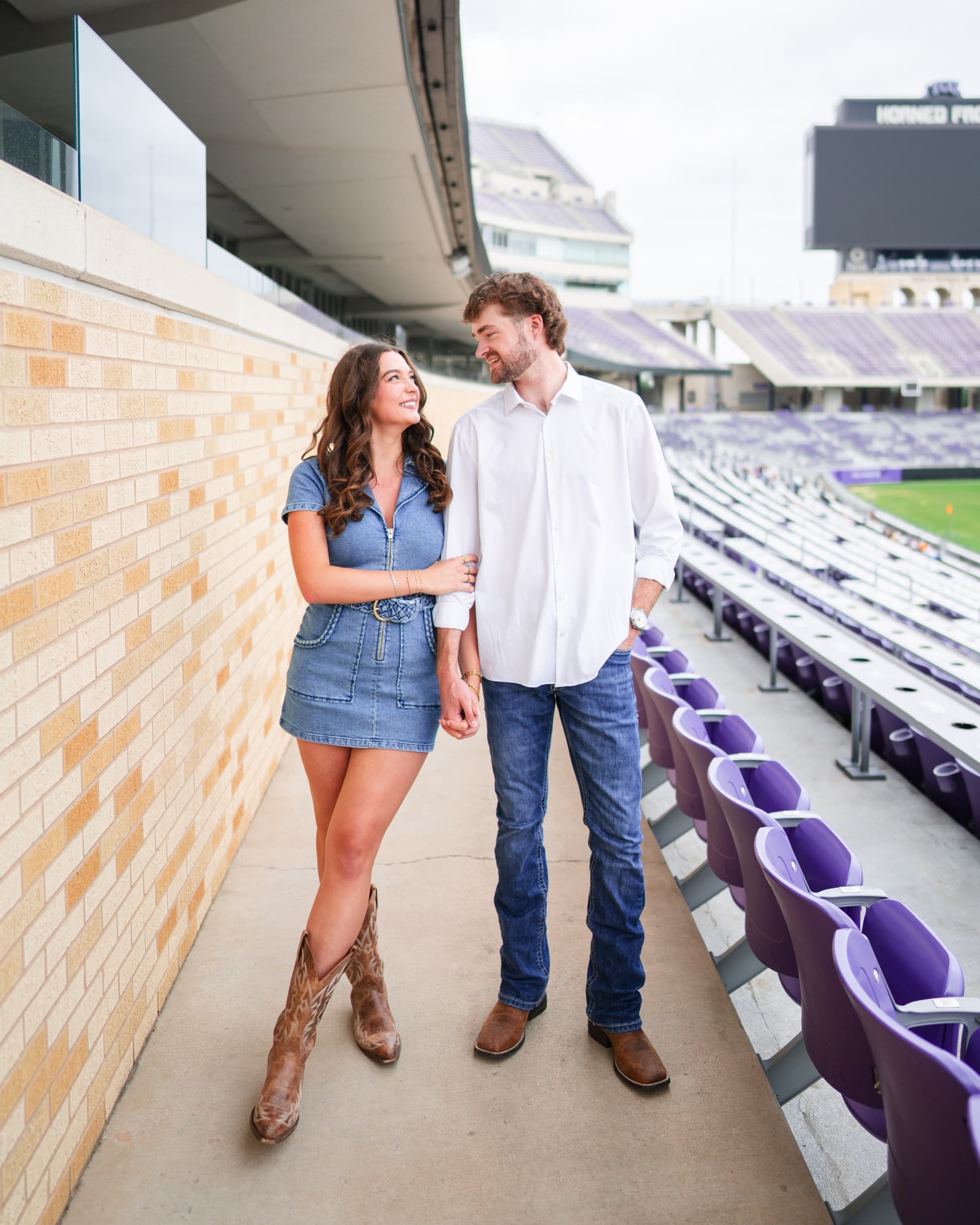 Couple holding hands and smiling at each other, walking through a stadium seating aisle.