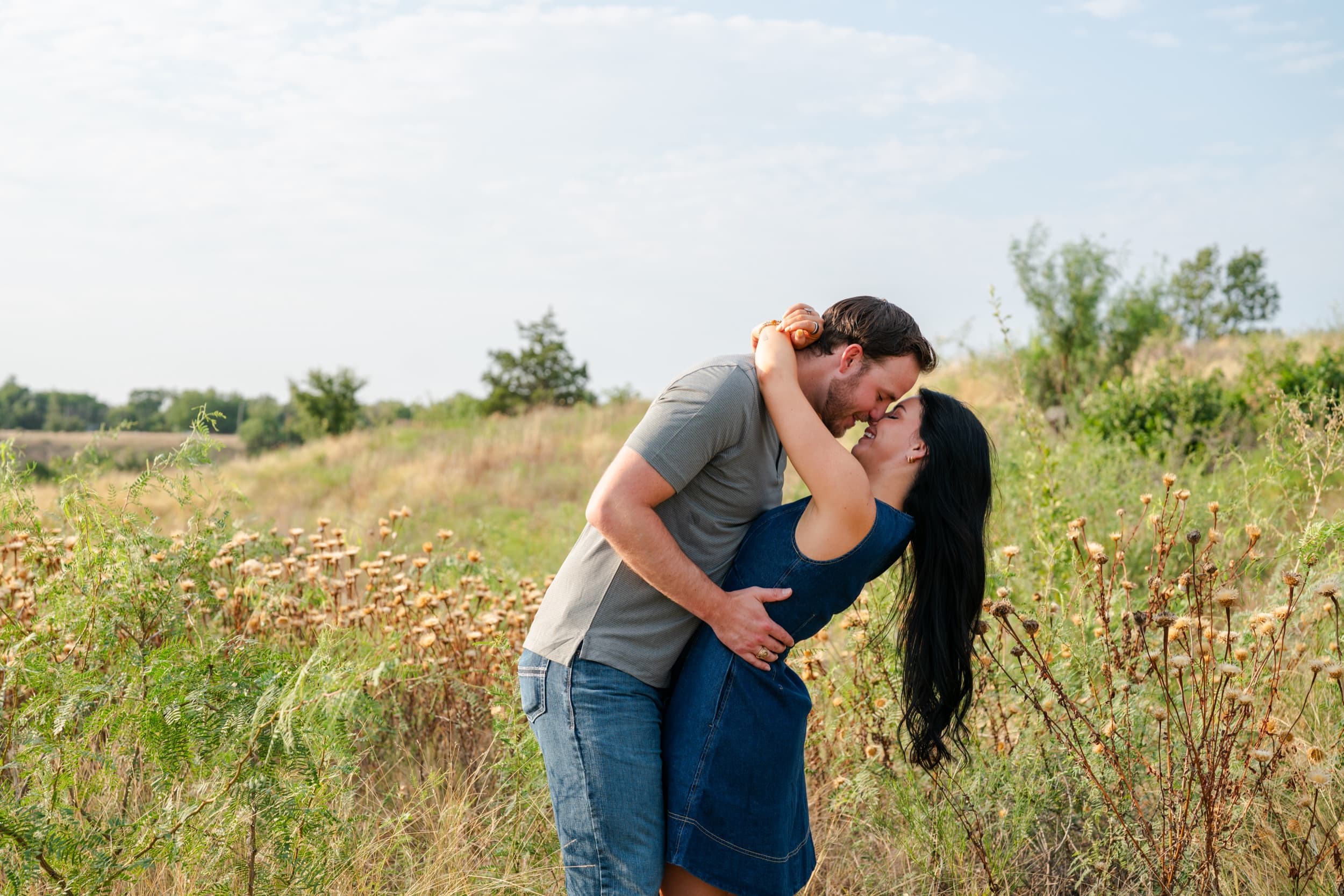 Couple leaning in for a kiss in a wildflower field, her arms wrapped around his neck.