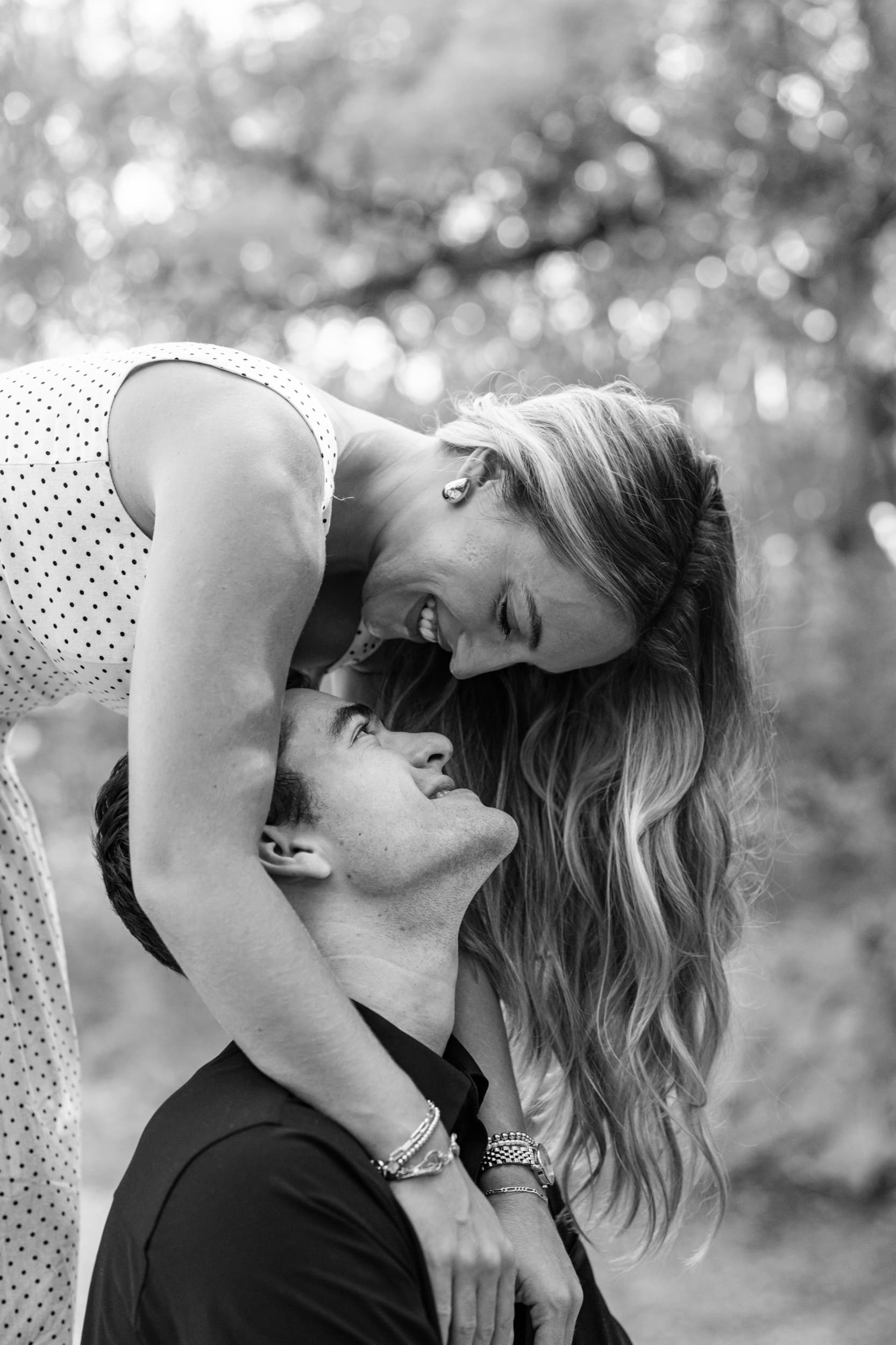 Black and white photo of a laughing woman bending down to a man looking up at her in an embrace.