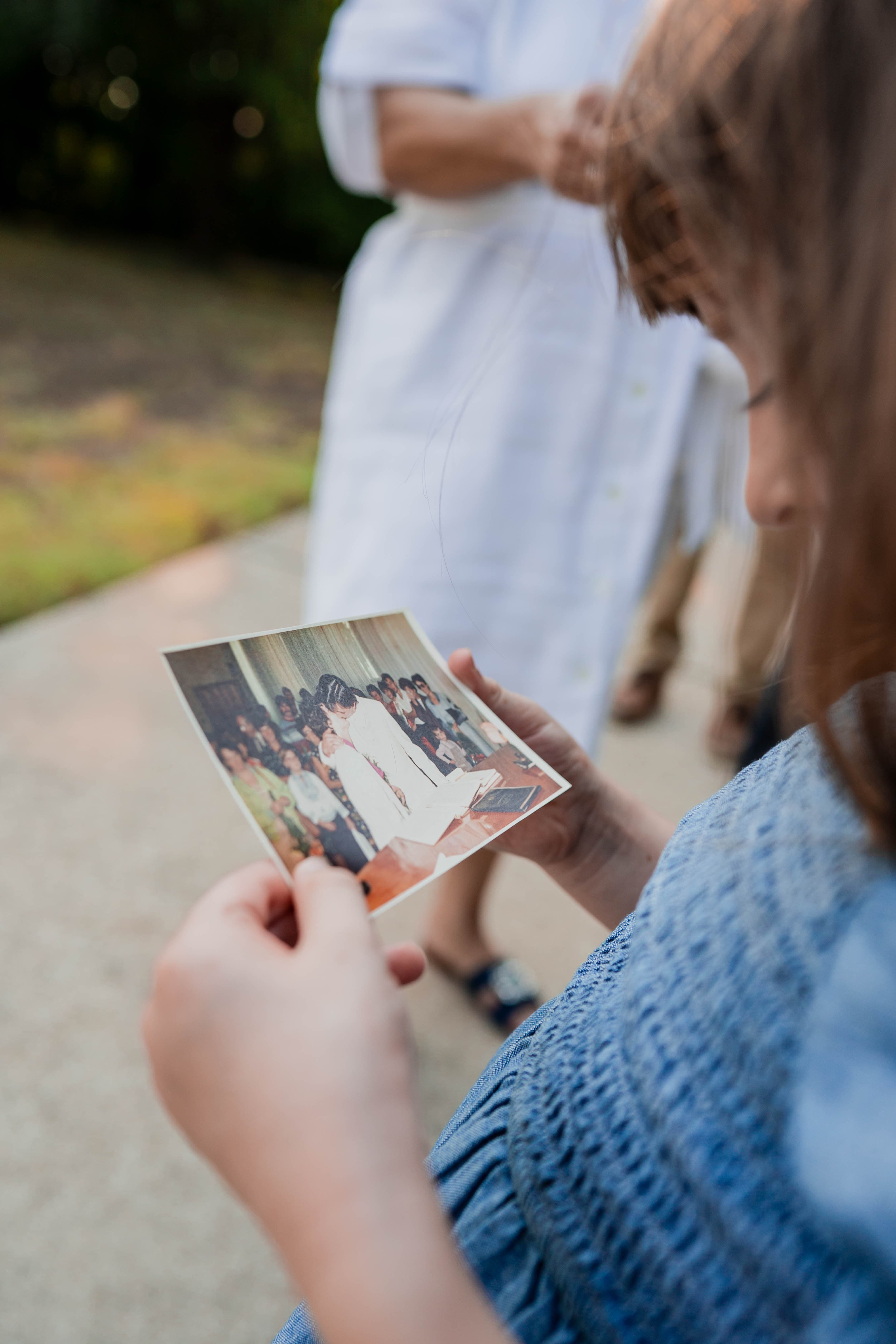 Woman looking at an old family photograph while a relative in white stands nearby.
