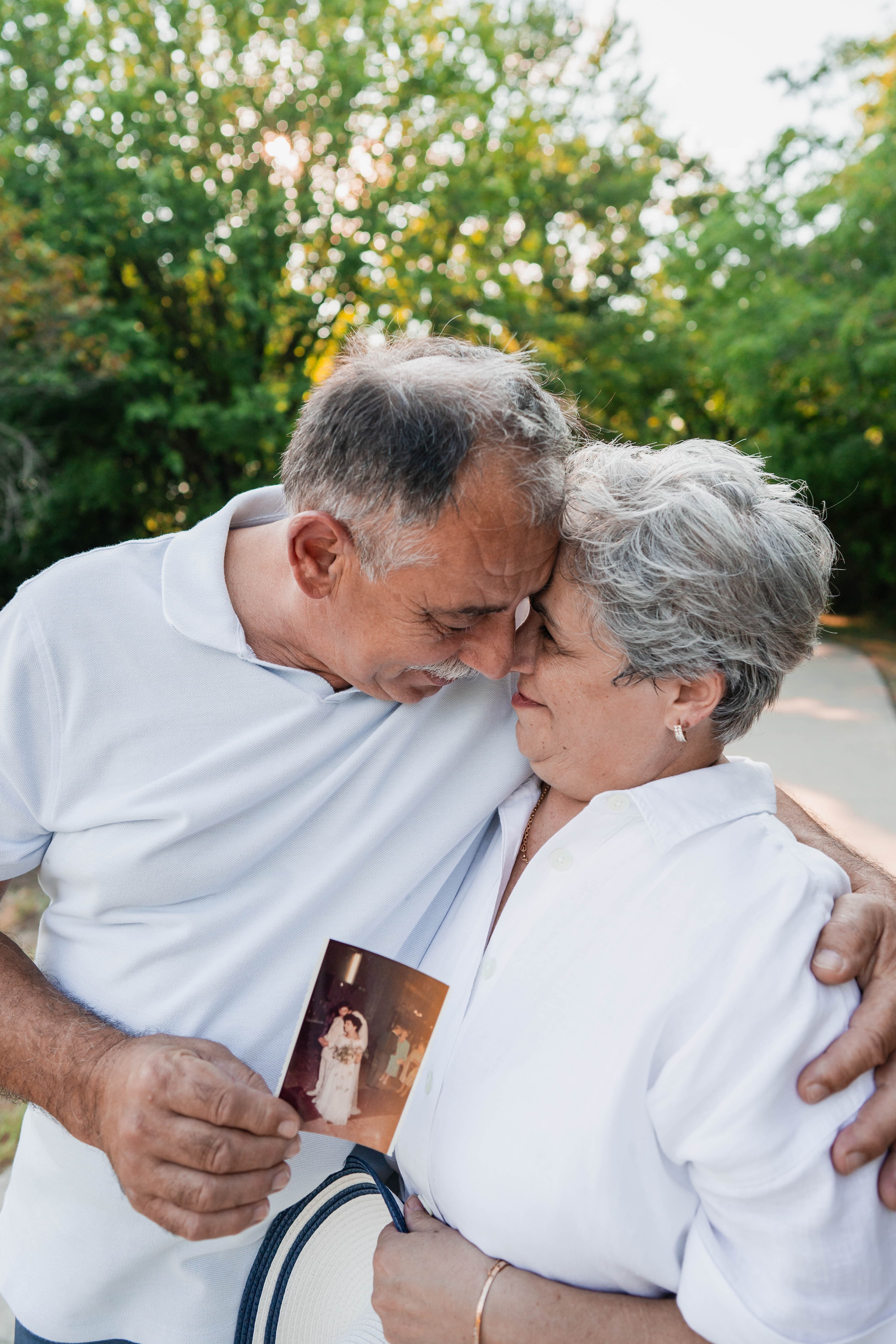 Grandparents embracing forehead to forehead, holding an old wedding photo between them.