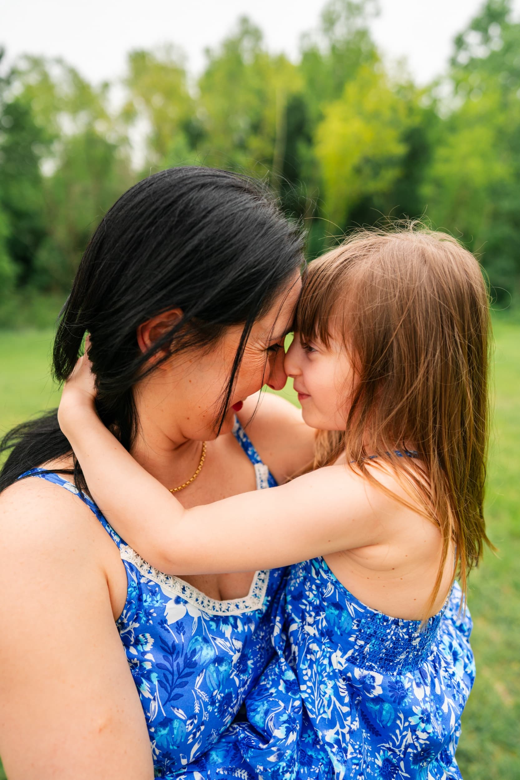 Mother and daughter in matching blue dresses touching foreheads in a tender embrace.