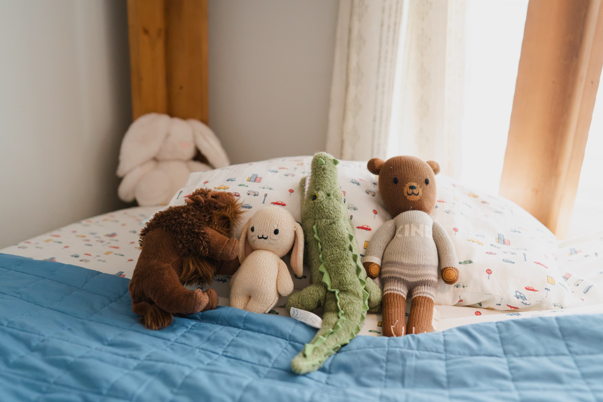 Row of stuffed animals — a lion, bunny, alligator, and bear — lined up on a bed.