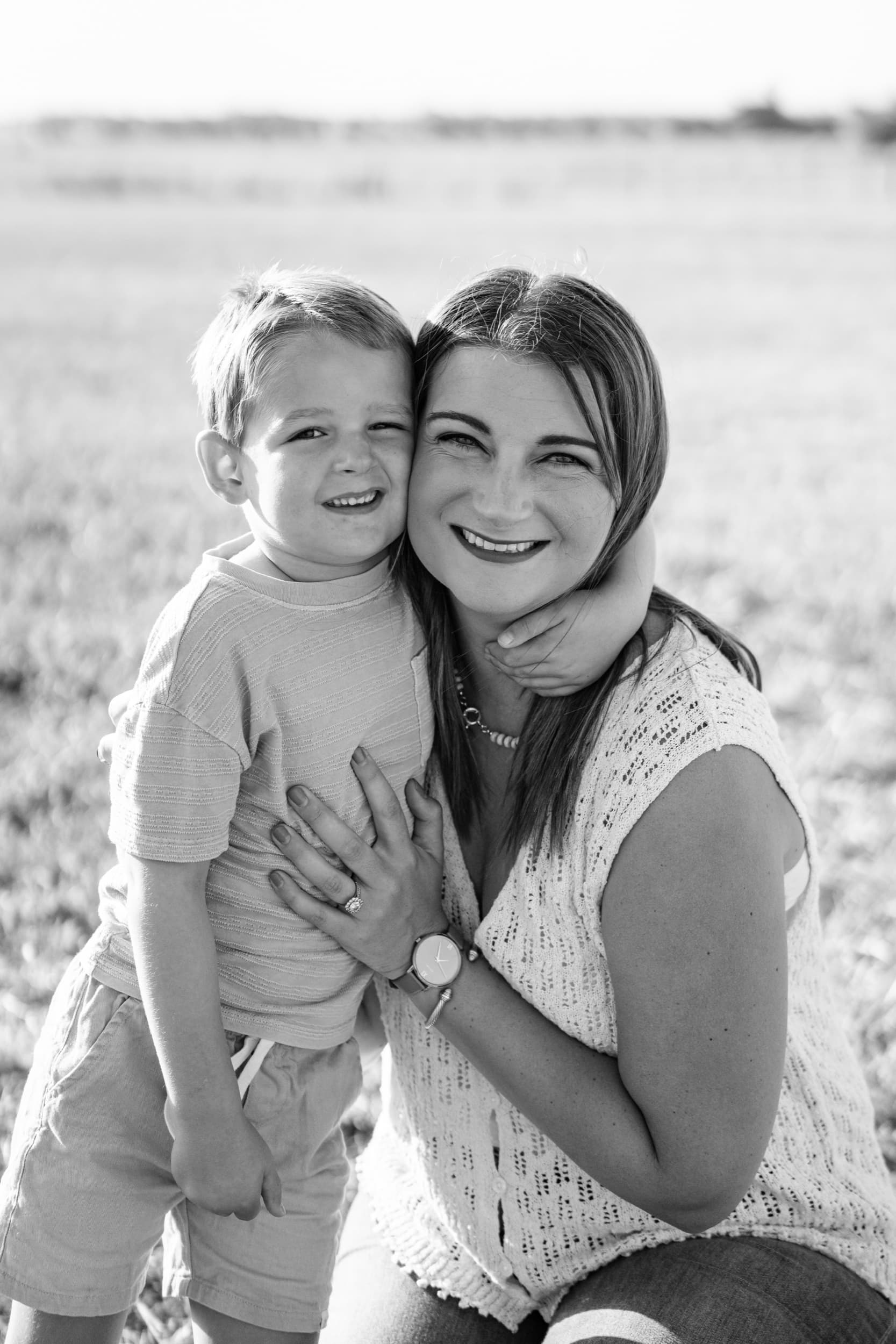 Black and white photo of a mother and son smiling cheek to cheek in an open field.