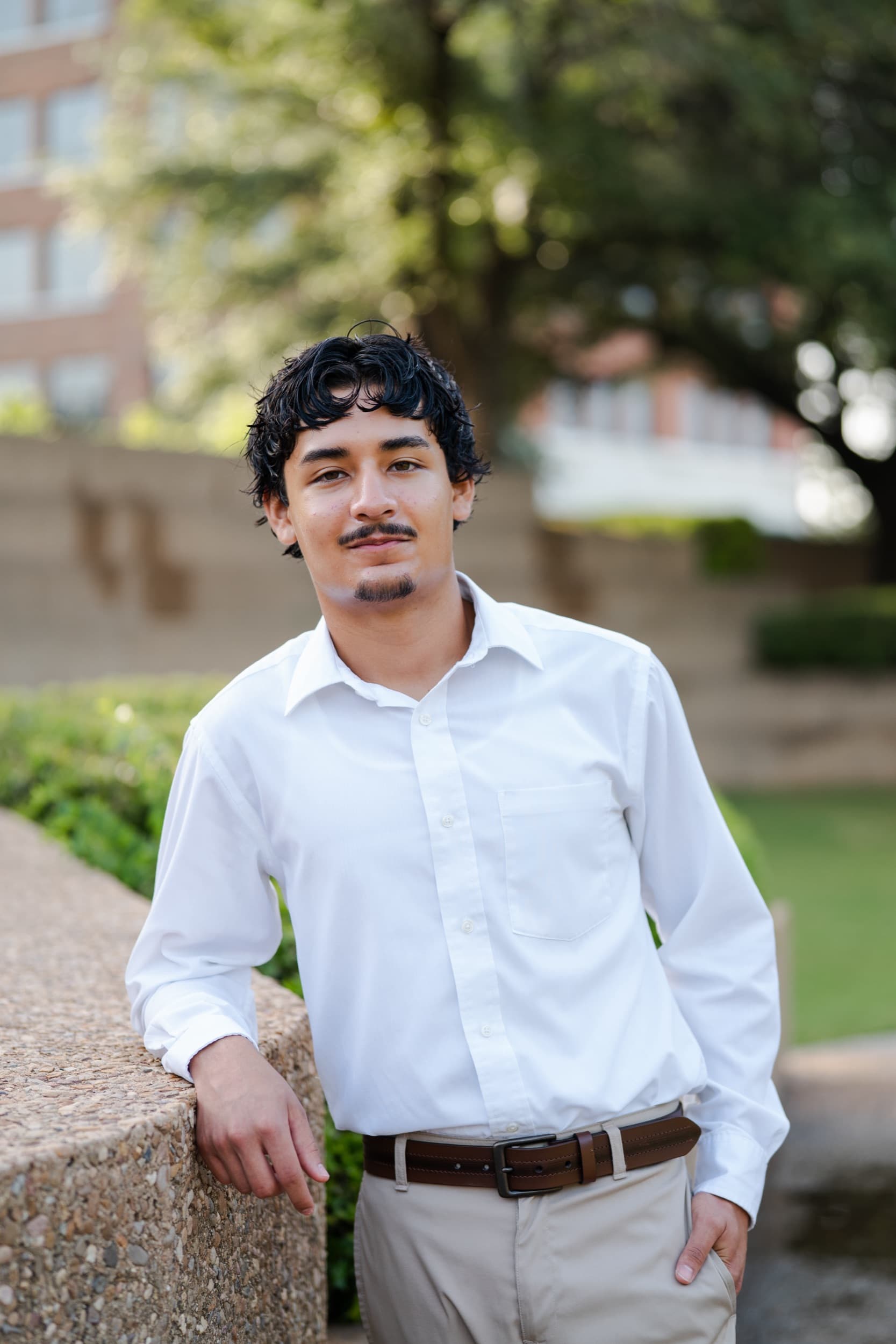 Senior in a white button-up leaning on a stone ledge in a garden.