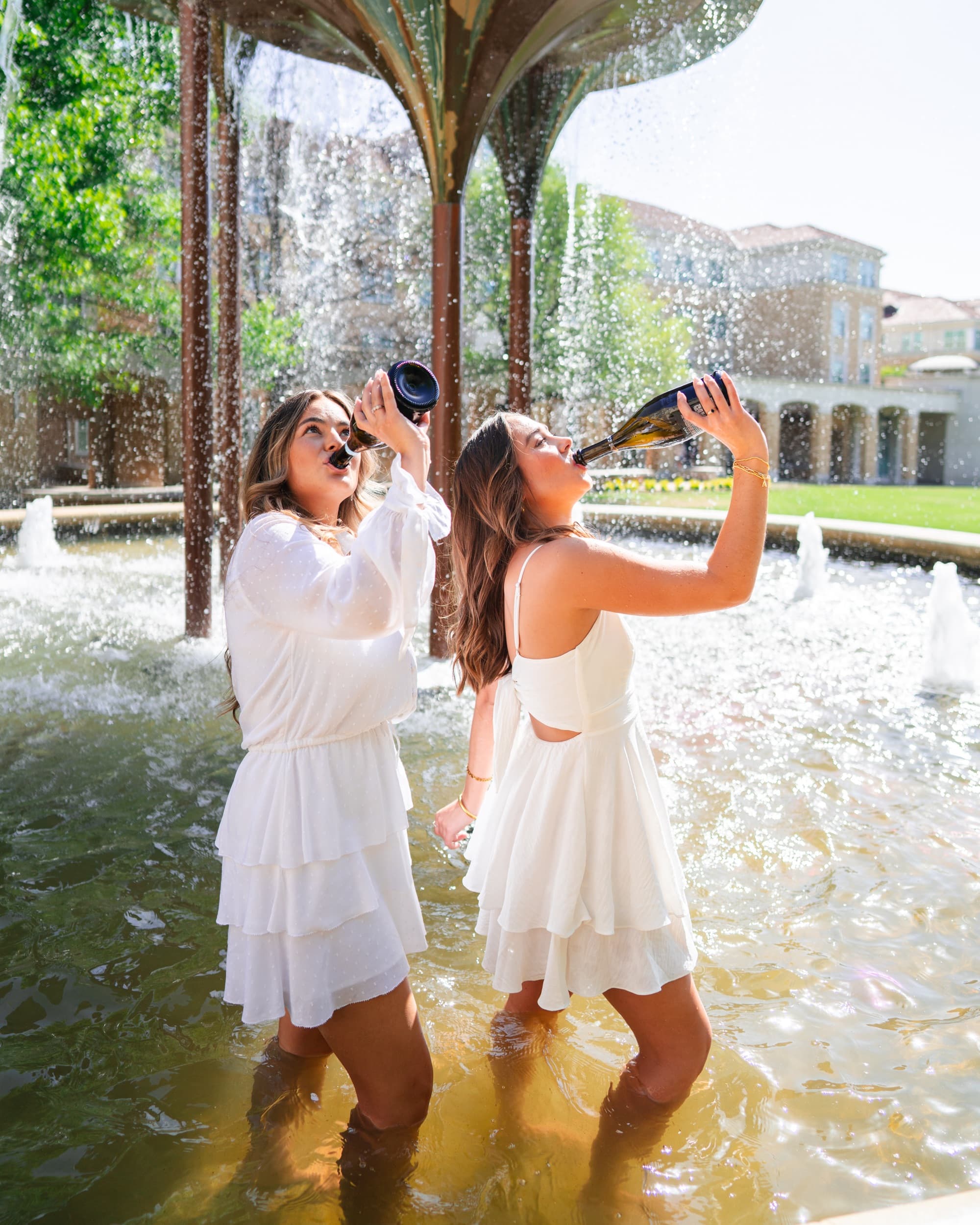 Two friends standing in a fountain, sipping drinks together in playful celebration.
