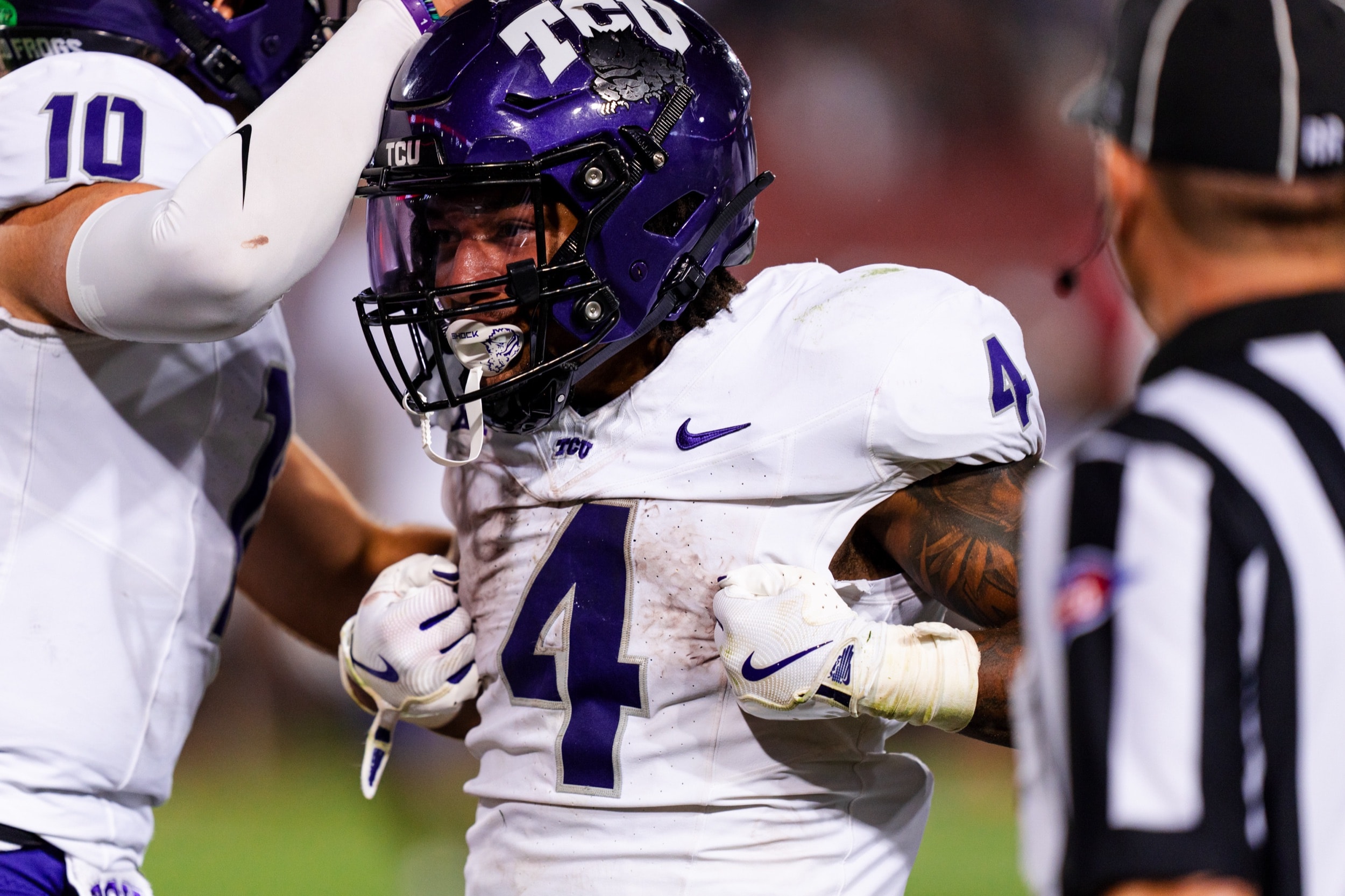 Football player in a muddy jersey flexing intensely on the field during a night game.