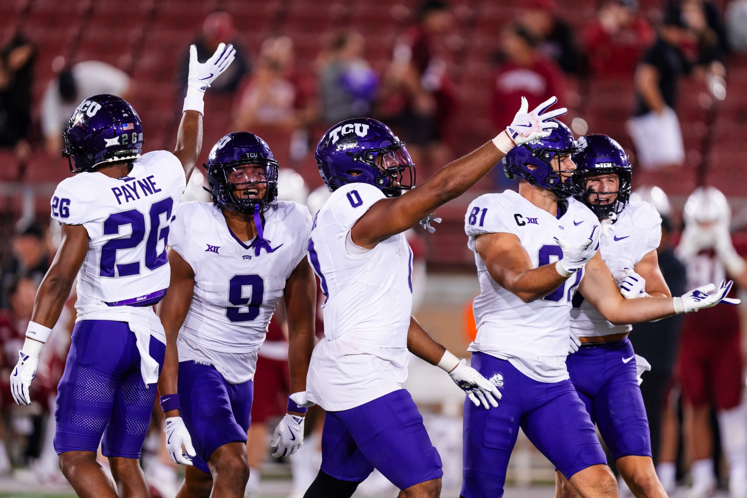 Group of football players in white jerseys celebrating with raised arms during an evening game.