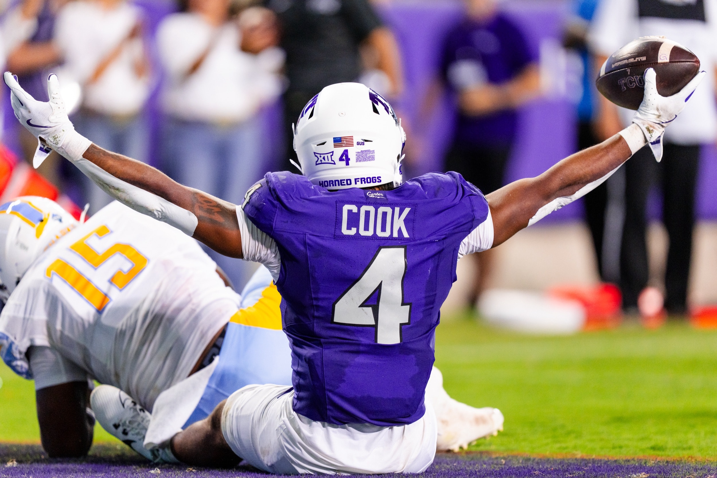 Football player sliding on his knees, arms spread wide, celebrating a touchdown catch.