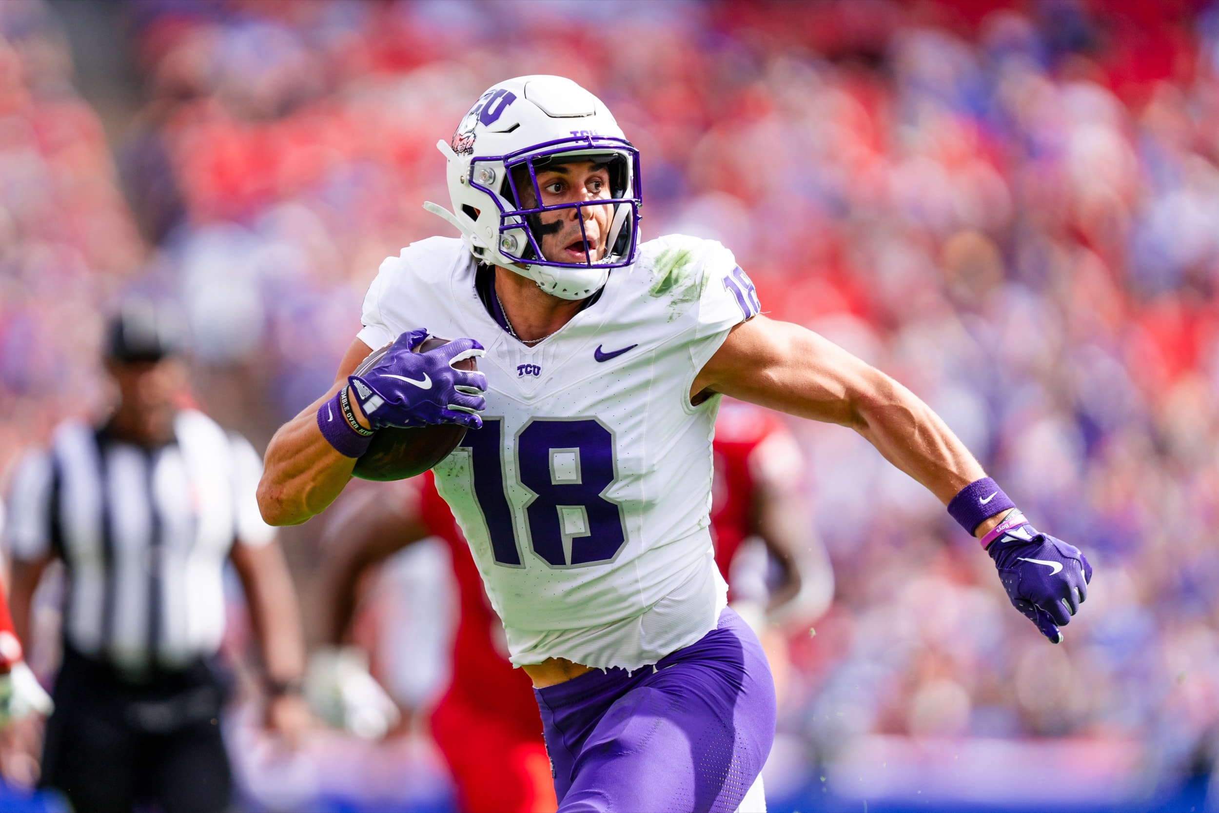 Football player sprinting downfield with the ball tucked tightly, focused expression on his face.