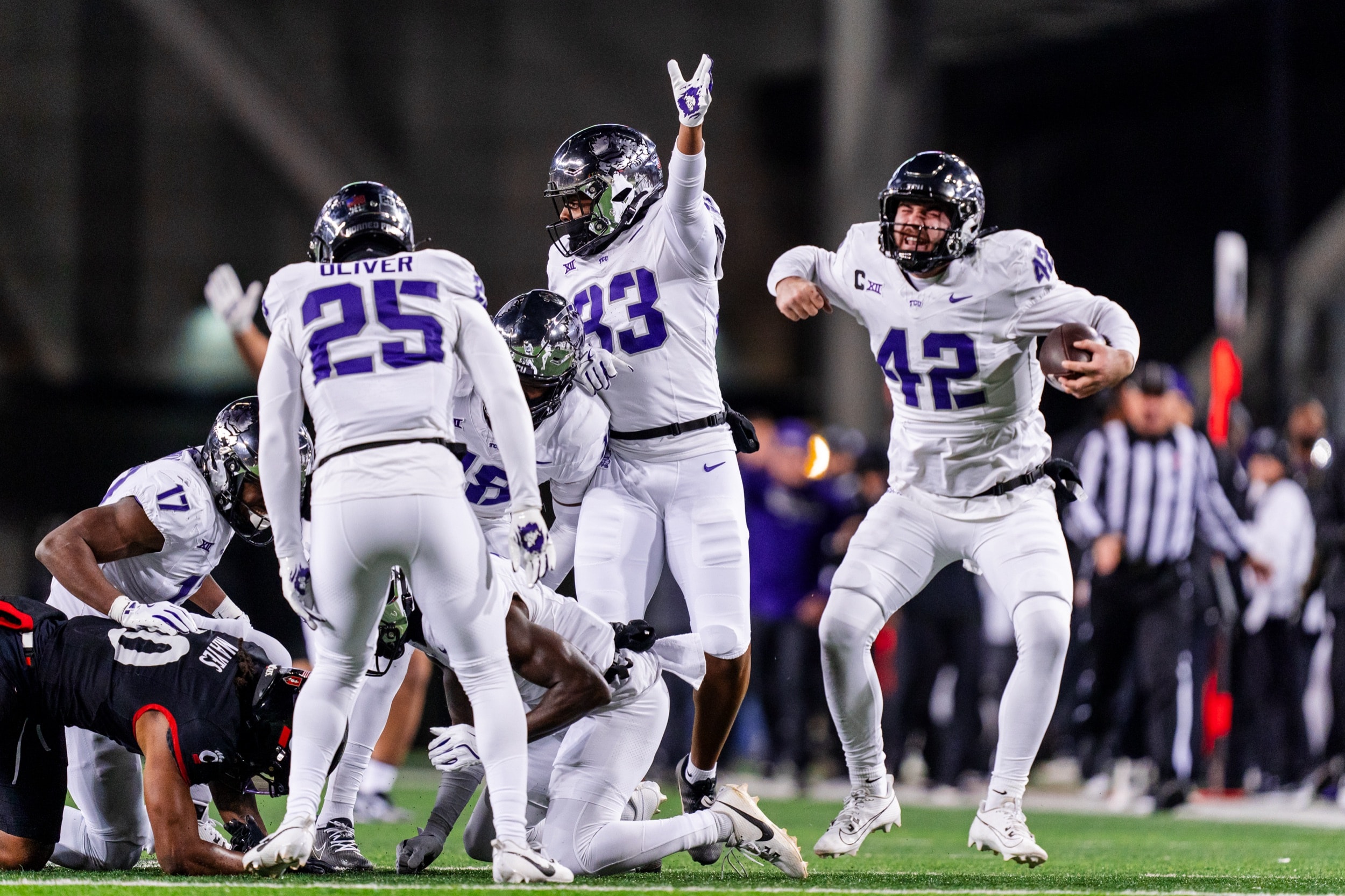 Defensive players celebrating a turnover recovery, shouting and cheering under bright stadium lights.
