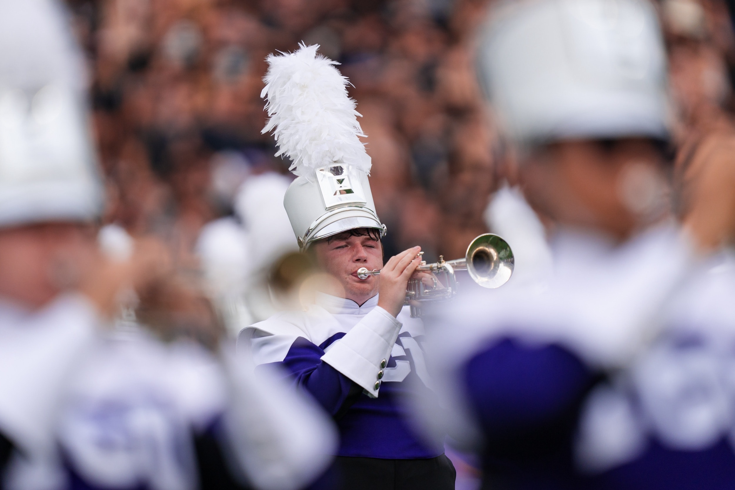 Marching band trumpet player performing intently in a plumed hat, framed by fellow musicians.