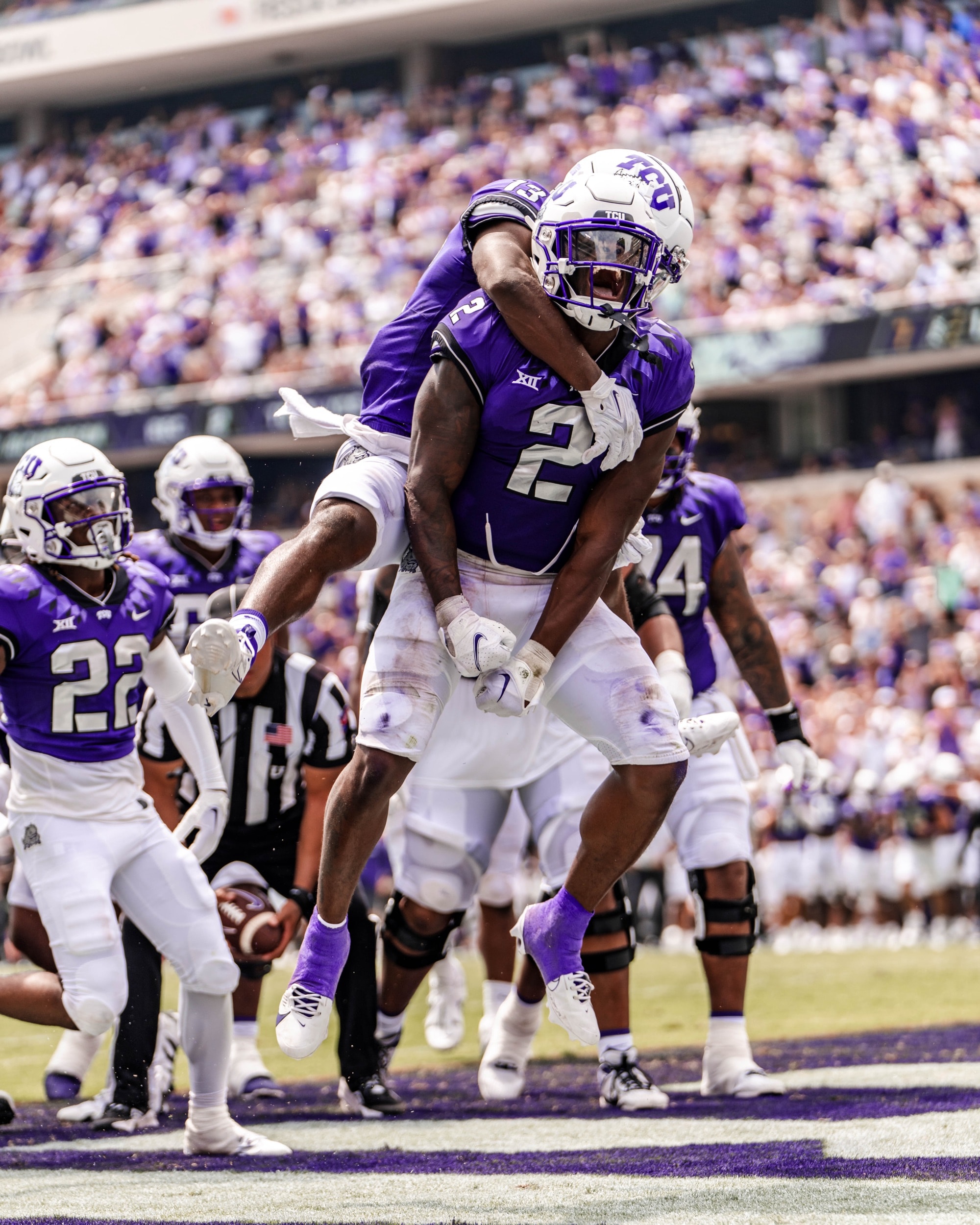 Football players celebrating a touchdown, one leaping onto the other's back in the end zone.